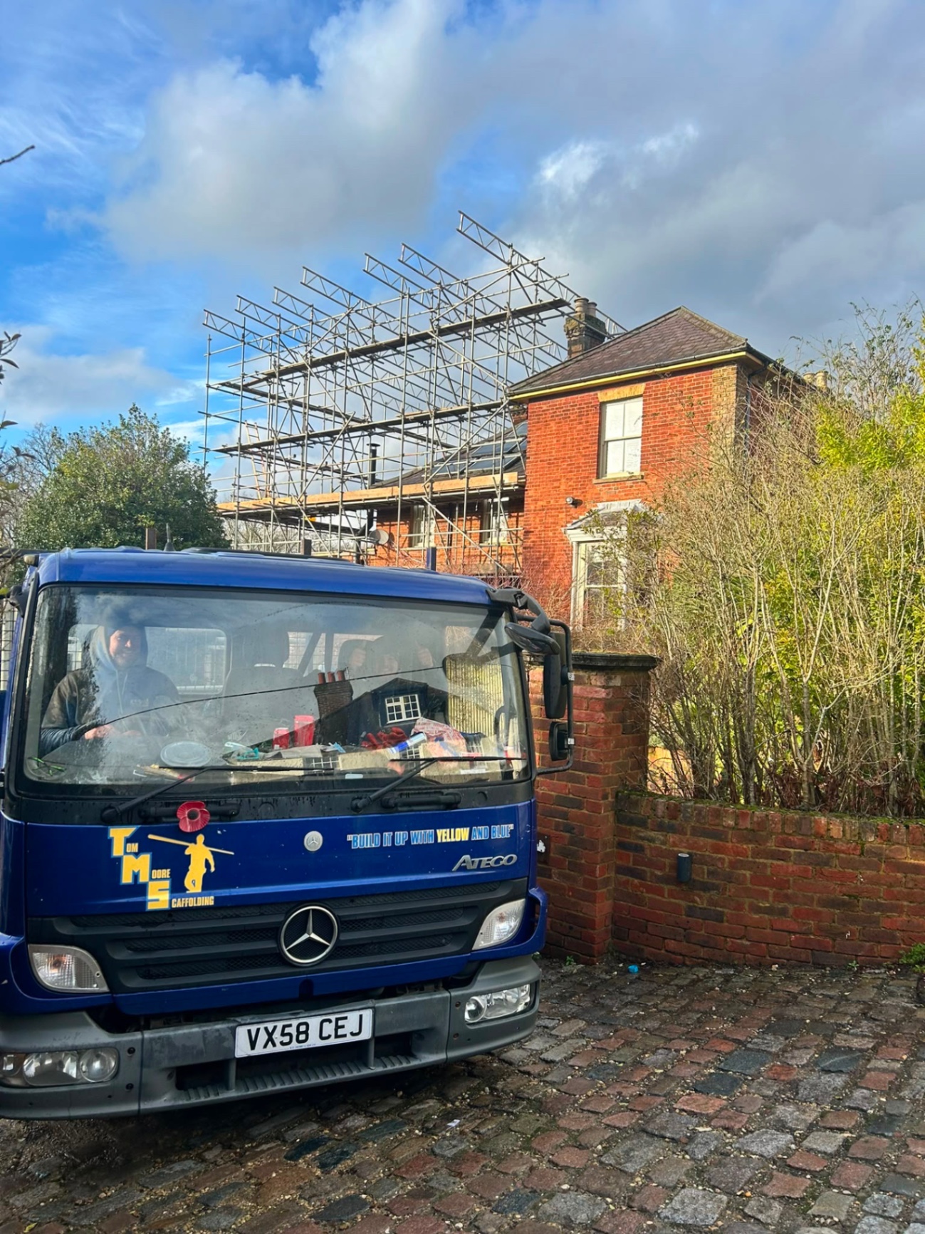 Blue Tom Moore Scaffolding truck parked beside a period house with a temporary roof scaffold